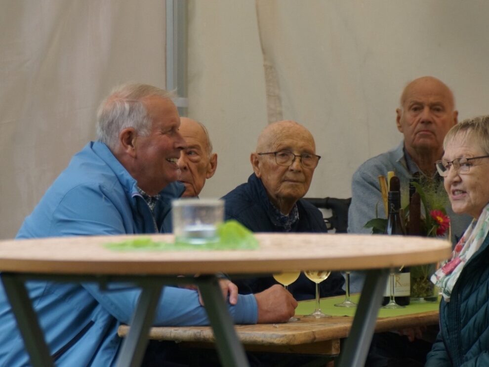 Mehrere Gäste sitzen mit Weinflaschen und Gläsern gemeinsam an einem Tisch im Festzelt.