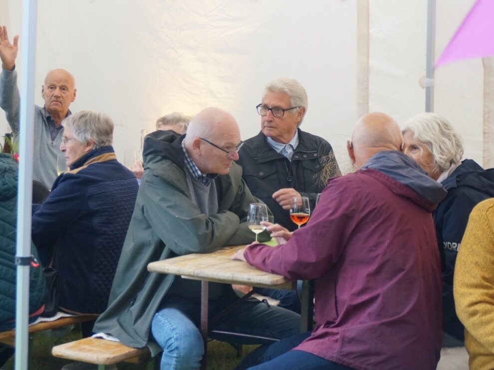 Gäste sitzen mit Wein und Blumenschmuck an einer langen Tafel im Festzelt.