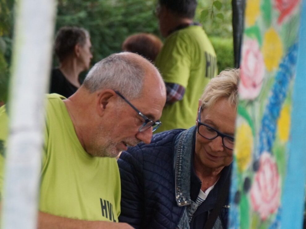 Ein Helfer und eine Besucherin betrachten gemeinsam etwas neben einer farbigen Dekoration.