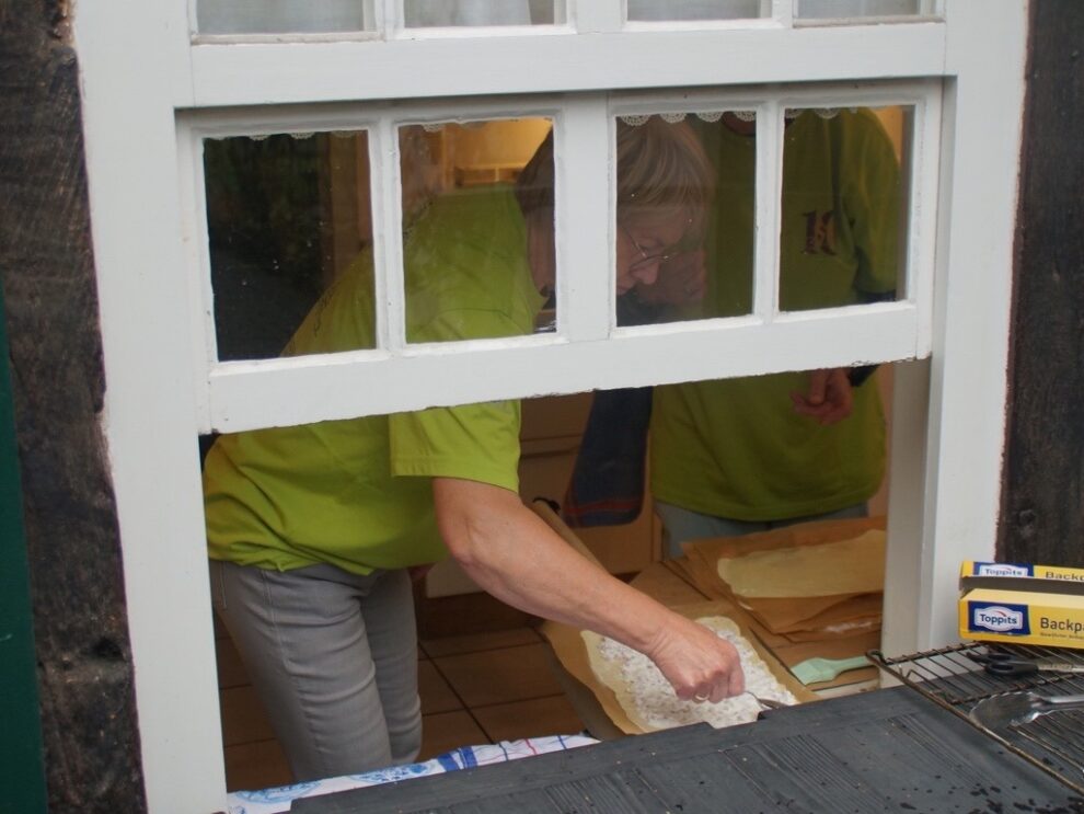 Helferinnen belegen in der Küche Teigfladen, gesehen durch ein geöffnetes Fenster.