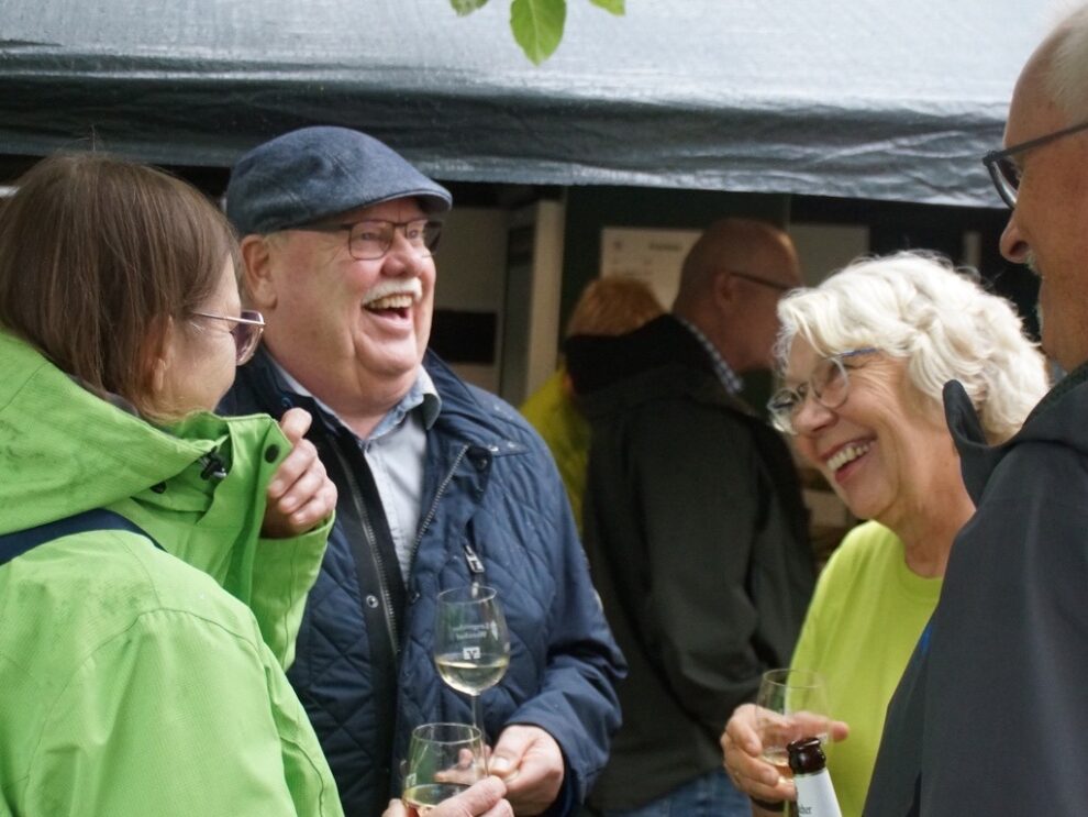 Eine Helferin und mehrere Gäste lachen gemeinsam mit Wein- und Biergläsern.