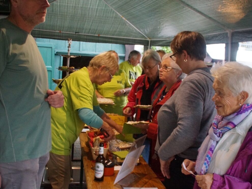 Helferinnen bedienen eine Gruppe von Besucherinnen am Gebäckstand.