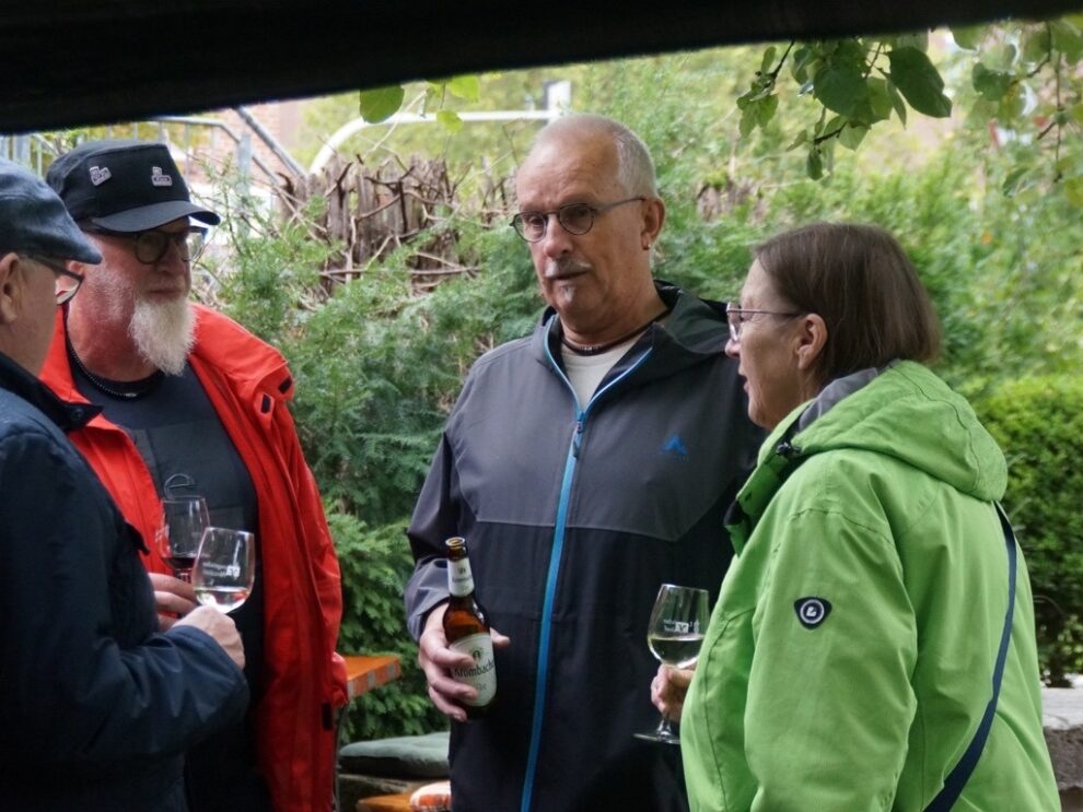 Vier Gäste unterhalten sich im Freien mit Wein- und Biergläsern.