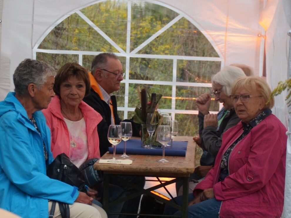 Fünf Gäste sitzen mit Weingläsern gemeinsam an einem Tisch im Festzelt.
