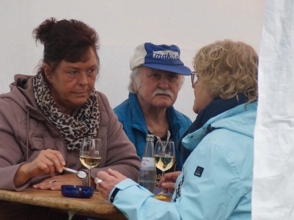 Zwei Frauen und ein Mann unterhalten sich mit Wein und Wasser an einem Tisch.