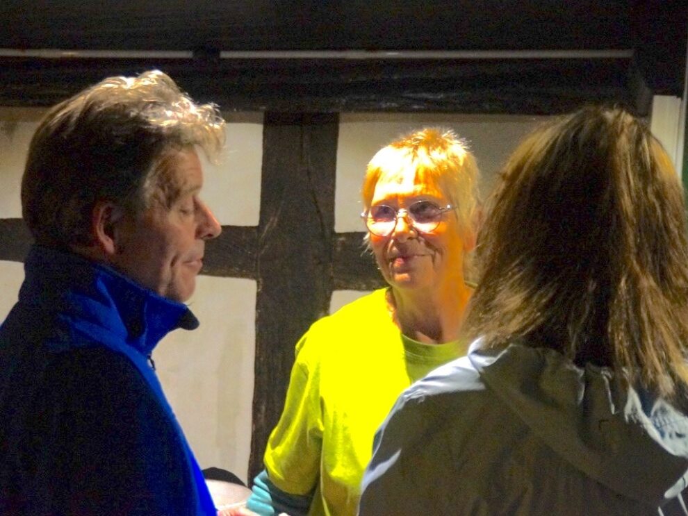 Eine Helferin spricht am Abend vor einem Fachwerkhaus mit zwei Besucherinnen.