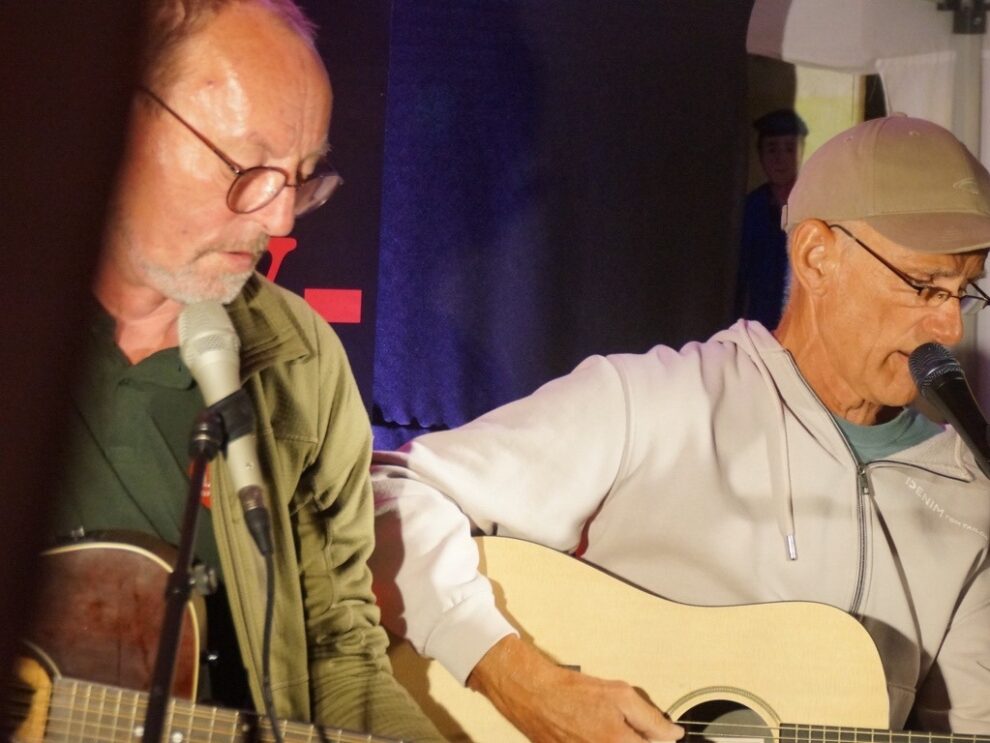 Zwei Musiker singen an Mikrofonen und begleiten sich auf Akustikgitarren.