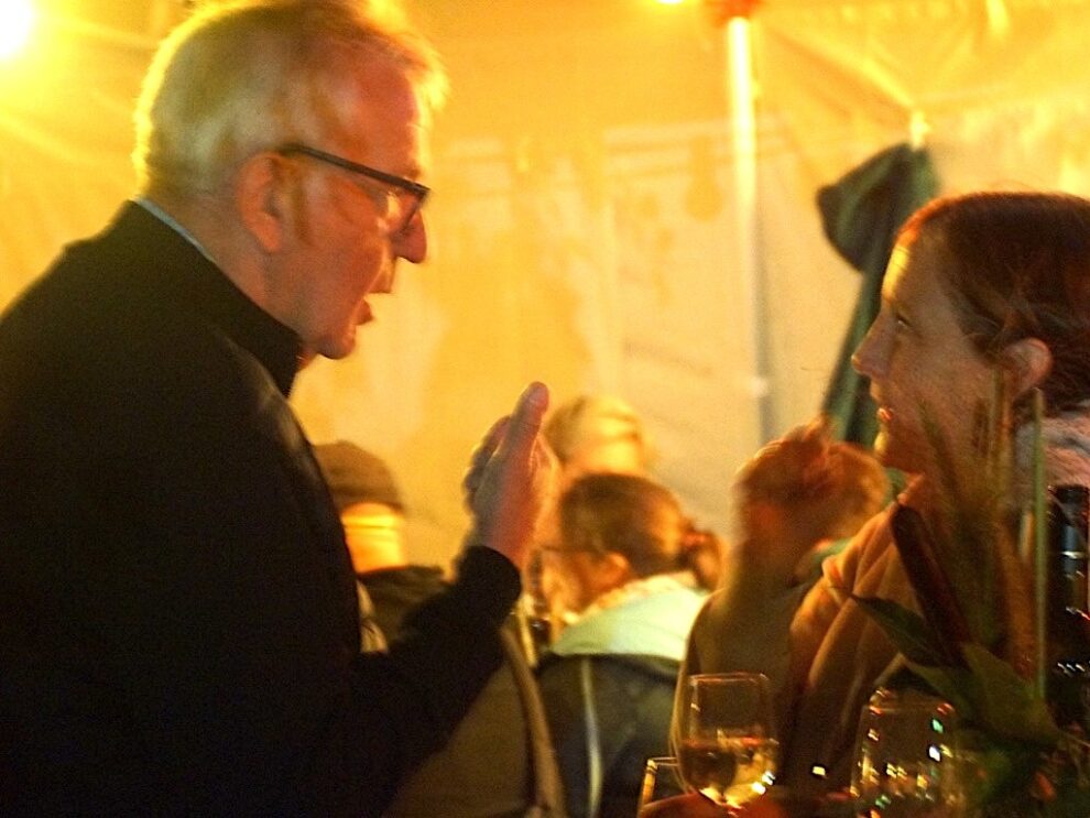 Ein Mann und eine Frau unterhalten sich angeregt in einem beleuchteten Festzelt.